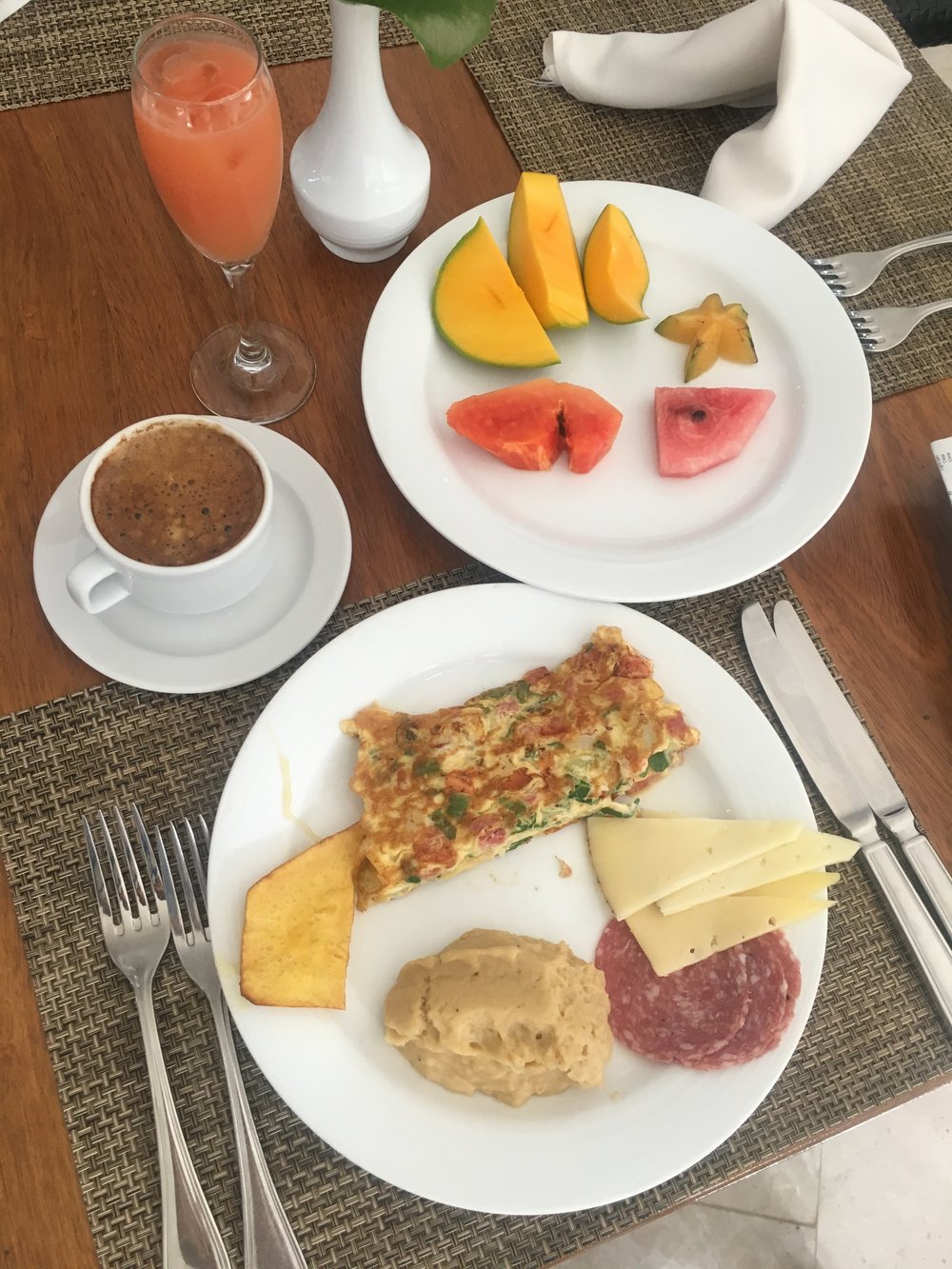 A vibrant breakfast spread with fresh mango, watermelon, and starfruit, alongside an omelet, cheese, hummus, and salami, paired with coffee and juice, embodying wholesome, nourishing, and healthy living with fresh flavors.| Daré Vita Café | Las Vegas