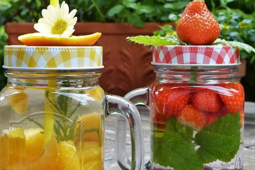 Two mason jars filled with vibrant, fresh fruit-infused water; one with orange slices and a daisy, and the other with strawberries and mint. These refreshing drinks exemplify healthy living with natural, allergen-friendly ingredients.| Daré Vita Café | Las Vegas