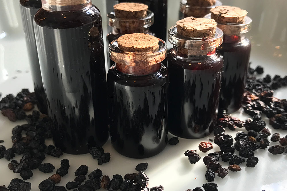 Dark glass bottles with cork stoppers are filled with a rich liquid, surrounded by dried berries on a reflective surface, suggesting a natural, wholesome essence. This scene emphasizes fresh ingredients and healthy living.| Daré Vita Café | Las Vegas