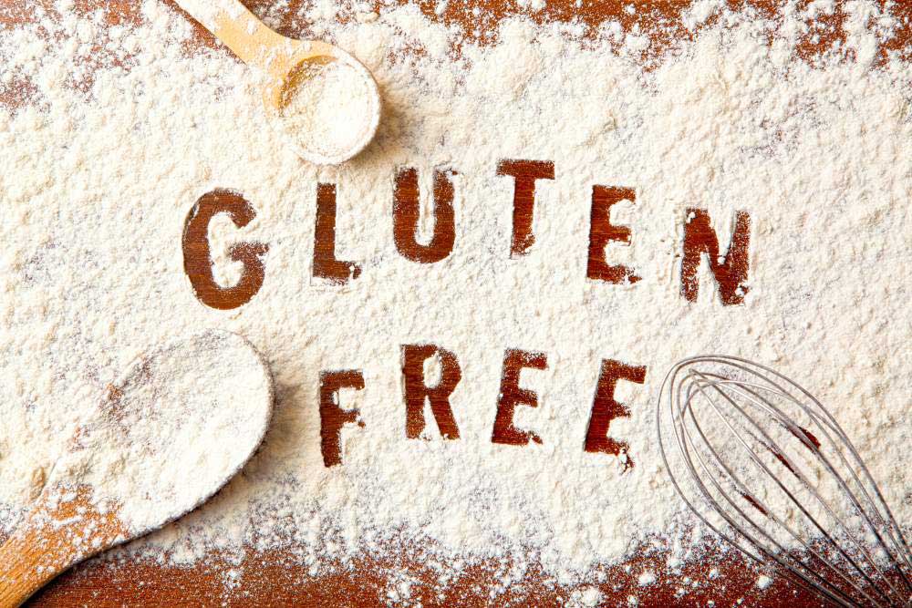 Gluten-Free-Wheat—Progress-or-Newest-Problem-3 The words "Gluten Free" are written in flour on a wooden surface, surrounded by a whisk and a spoon, emphasizing the allergen-friendly and wholesome nature of the ingredients used, ideal for those seeking healthy living and food sensitivity options.| Daré Vita Café | Las Vegas