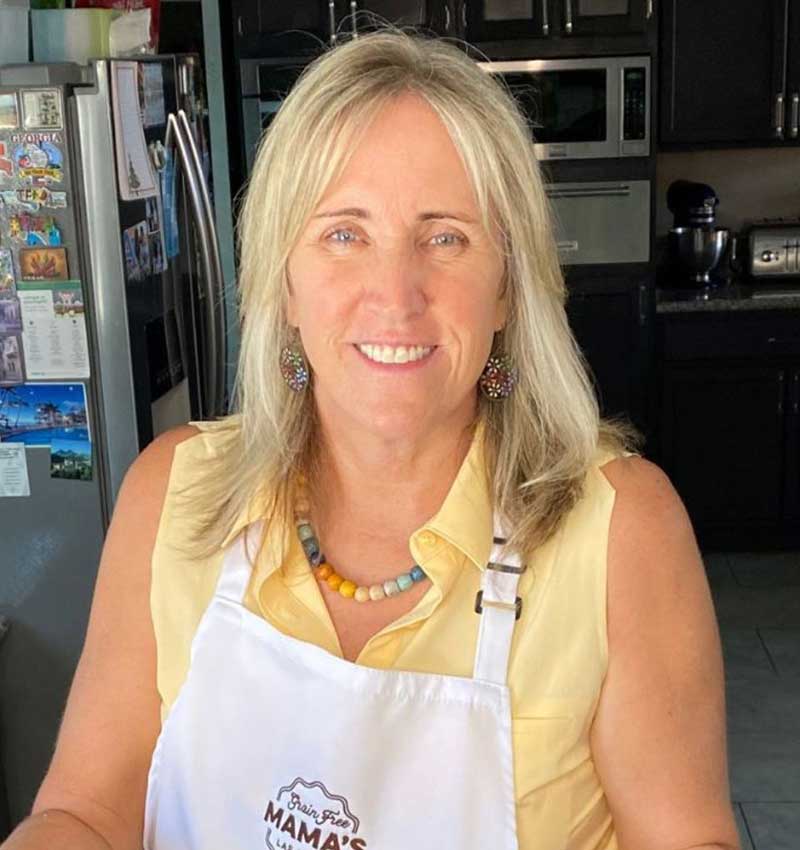 margie-placeholder-2 A smiling person wearing a yellow shirt and white apron stands in a kitchen with a fridge in the background, embodying a healthy living lifestyle focused on natural and allergen-friendly cooking.| Daré Vita Café | Las Vegas
